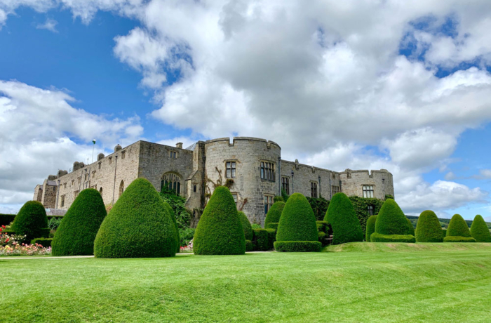 Chirk Castle in Wales with green grass, manicured hedges and white clouds in the blue sky.